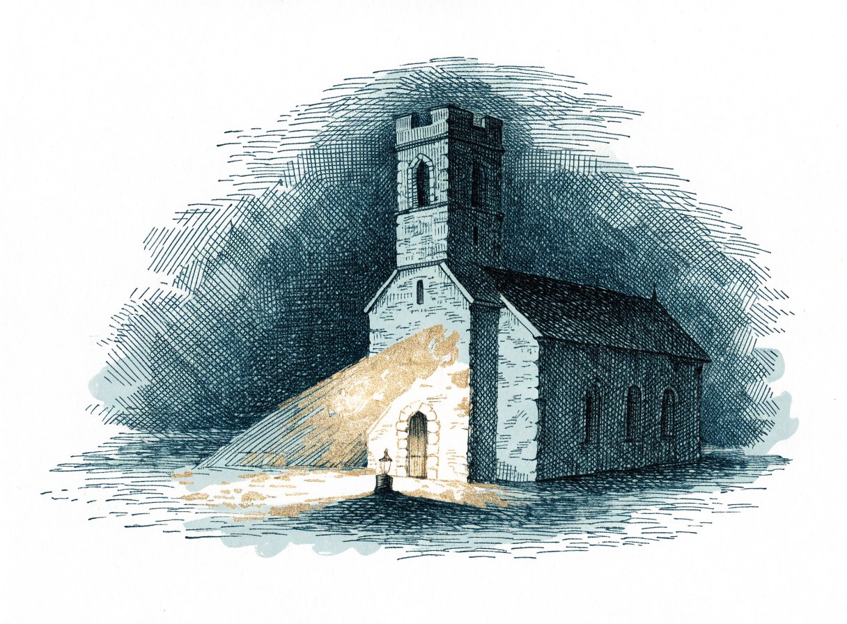 A stone church at night, its front washed in gold light from a small lantern set on the ground before it